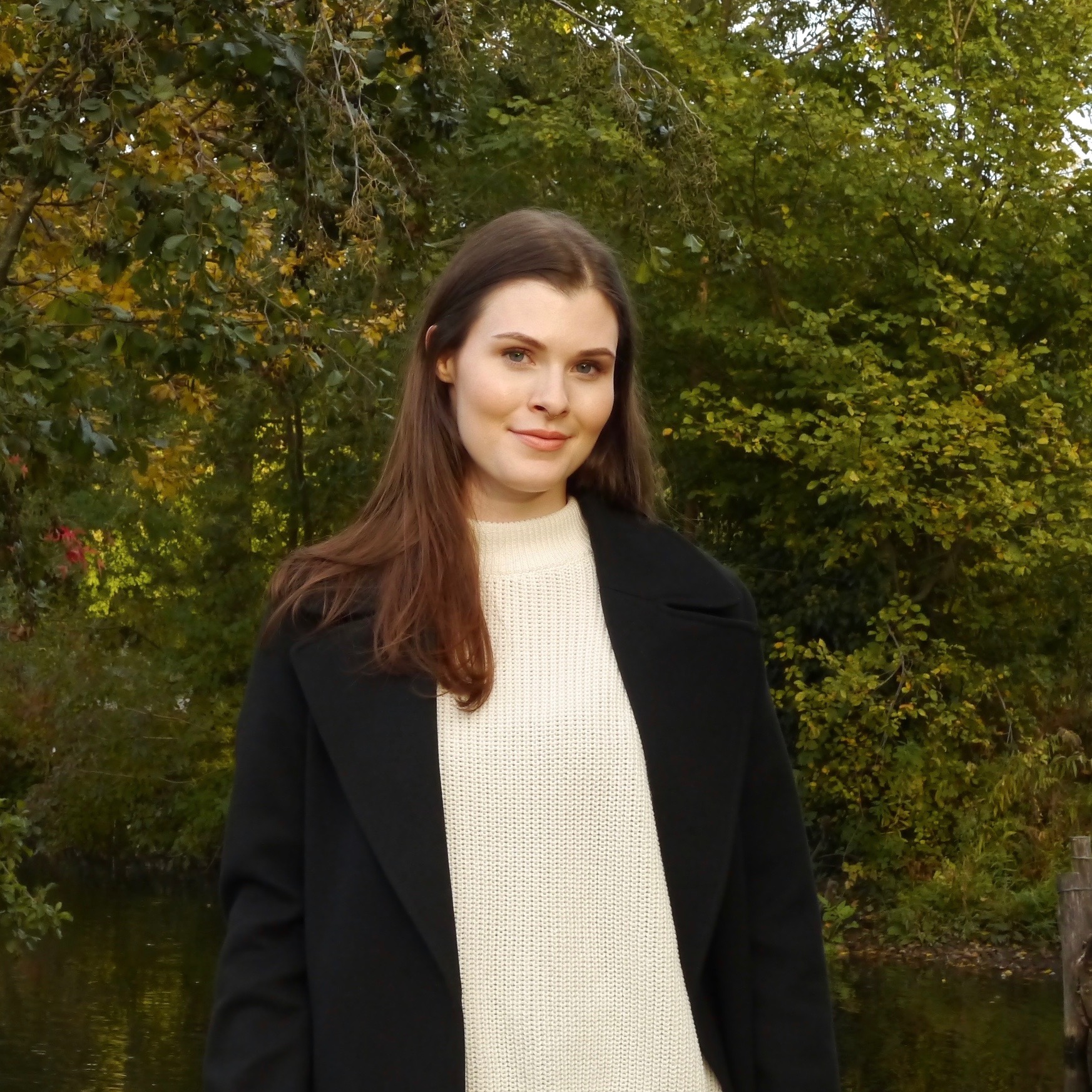 A picture of a young woman with brown hair smiling and wearing a dark coat and a white knit jumper